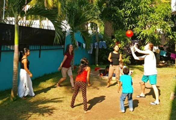 Several adults playing game with children in the shade